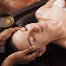 Ayurvedic face massage with oil on the wooden table AWE Cosmeceuticals
