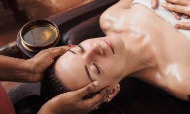 Ayurvedic face massage with oil on the wooden table AWE Cosmeceuticals
